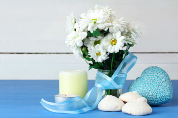 a bouquet of white daisies with candles and sweets around decorative hearts on a blue wooden table