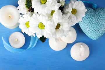 a bouquet of white daisies with candles and sweets around decorative hearts on a blue wooden table