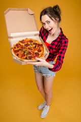 Beautiful smiling young woman standing and showing pizza