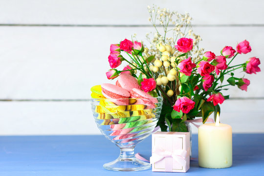 Macaroon in the ramekin next to the roses and gift on blue wooden background