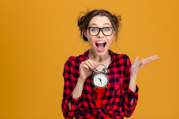 Amusing pretty young woman holding alarm clock and shouting