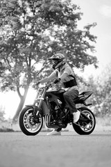 Love riding. Monochrome vertical shot of a biker man in a helmet sitting on a bike on the road