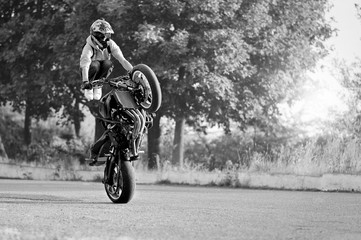 You should try this sport. Black and white soft smudged focus shot of a young biker man wearing protection gear during a stunt on his motorbike