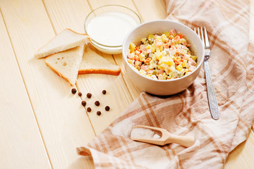 
Russian salad with potatoes , sausage , carrot , egg and green peas , mayonnaise or sour cream and spices on a wooden background