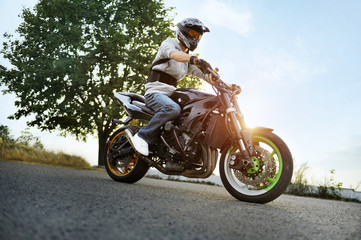 Fototapeta na wymiar Sunset ride. Extreme stuntman sitting on a motorcycle on the road during beautiful sunset