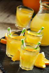 Orange drink in small glasses with striped straws and pitcher, s