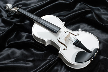 Closeup of a white violin on a background of  black satin