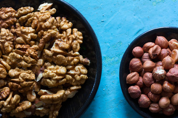 Part of the round wooden plates with the cleared walnuts and hazelnuts on a blue background.