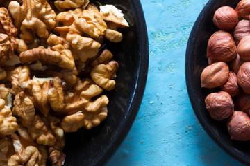 Part of the round wooden plates with the cleared walnuts and hazelnuts on a blue background.