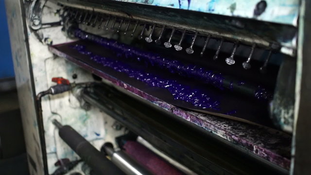 Closeup handheld shot of the blue or cyan ink or paint reservoir on a large industrial offset printing press.