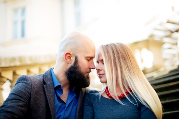 One beautiful stylish couple of young woman and senior man with long black beard sitting embracing close to each other outdoor in autumn street on stairs sunny day, horizontal picture