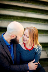 Fototapeta premium One beautiful stylish couple of young woman and senior man with long black beard sitting embracing close to each other outdoor in autumn street on stairs sunny day, horizontal picture