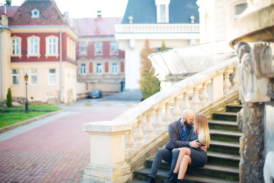 One beautiful stylish couple of young woman and senior man with long black beard sitting embracing close to each other outdoor in autumn street on stairs sunny day, horizontal picture