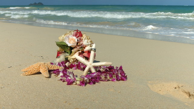 Wedding rings on the starfish, Lei and bouquet,  beach love concept. Closeup of two bands in flower heart for casual marriage celebration Oahu Hawaii.