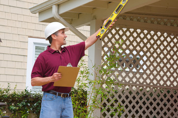 A home inspector or house building repair contractor in a hard hat holding a level and a clipboard...