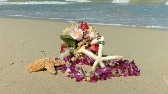 Wedding rings on the starfish, Lei and bouquet,  beach love concept. Closeup of two bands in flower heart for casual marriage celebration Oahu Hawaii.