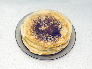 Stack of many fried pancakes on round  plate translucent dark color on the table. Photo closeup