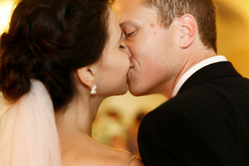 Handsome tender groom kissing emotional brunette bride closeup