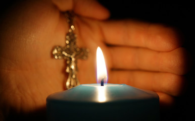 burning candle on background of hands with cross