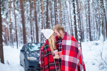 young couple sheltered red plaid holding a hot tea to the car in winter wood