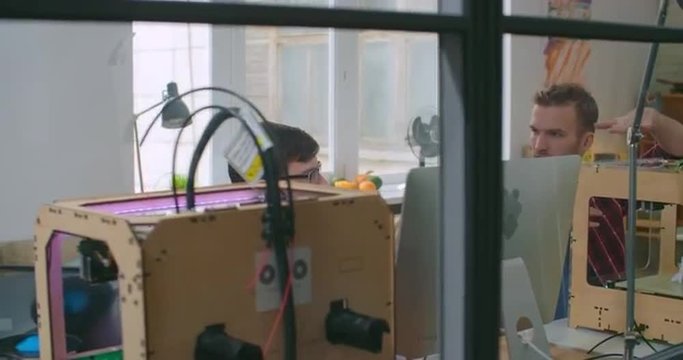 Panning shot of two young designers creating models for 3d printing via specialized software at studio