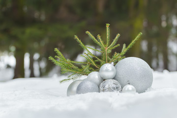 Small fir tree on snowy ground with Christmas bauble ornaments at bottom