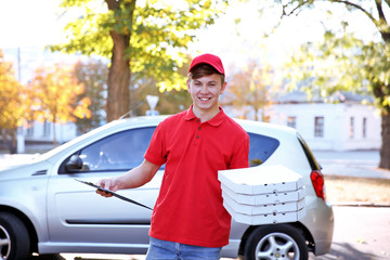 Pizza delivery boy holding boxes with pizza near car