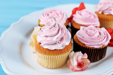 Tasty cupcakes on plate, on color wooden background
