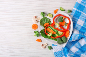 Useful cut vegetables on a plate in the form of heart on wooden table top view