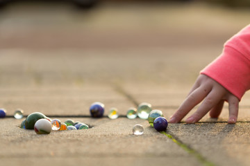 Child playing with marbles on yhe sidewalk.
old-fashioned toys still in use today.