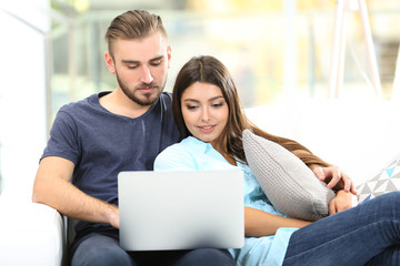 Happy couple sitting on sofa and working on a laptop