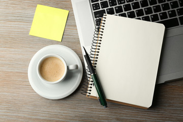Empty yellow adhesive paper, notebook on laptop keyboard, pen and coffee cup on desk background