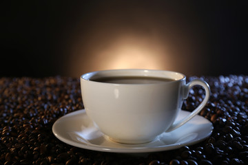 Cup of hot coffee among coffee beans on dark background