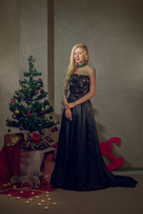 beautiful girl in long evening dress near christmas tree with gifts