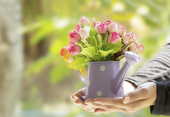 Colorful Artificial flowers in watering can with blurred backgro