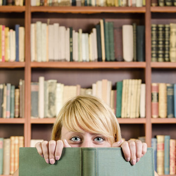 Girl hiding and smiling behind a book (square composition)