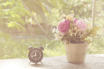 Black clock with  flowers in a basket on a wooden table in paste