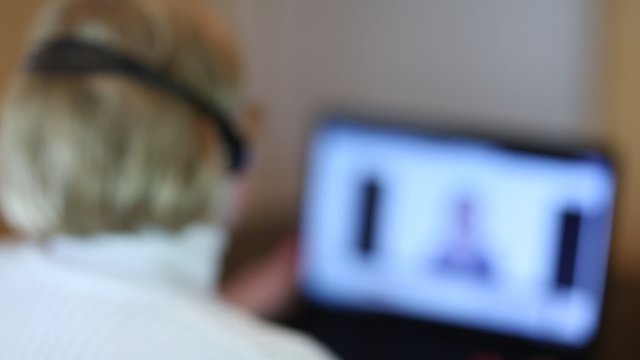 Woman with headphones with microphone talks to a customer via computer. Woman communicates via laptop. Senior woman with headphones and notebook speaks with customer