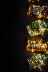 Winter holiday background: vintage vases and Christmas lights, decoration on black background. Top view, copy space.