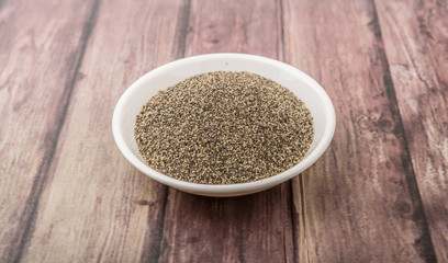 Black pepper powder in white bowl over wooden background