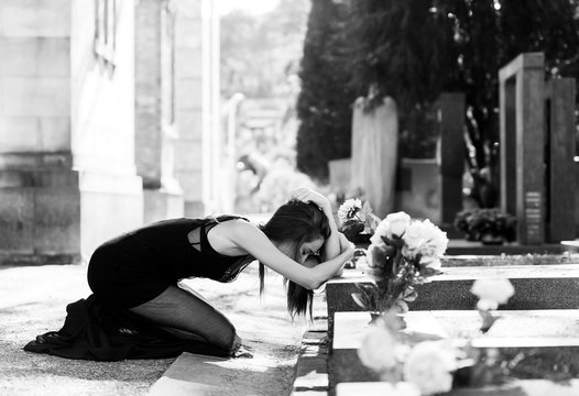Afflicted woman in grief in front of grave monochrome