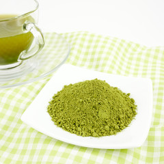The Japanese matcha green tea powder on mini white dish and the cup of Japanese tasty matcha green tea on green cotton fabric.