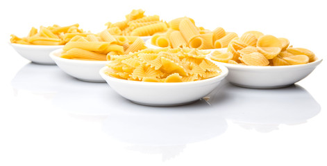 Dried pasta variety in shapes in white bowl over white background