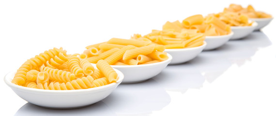 Dried pasta variety in shapes in white bowl over white background