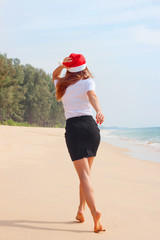 New Year holidays woman in office suit white blouse and a black skirt running down the beach in a red New Year's cap, hat, joy, from the back