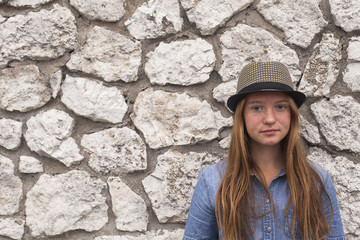 Girl with long beautiful hair with a hat, portrait near the stone wall.
