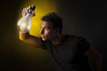 Concetto di pensiero ed immaginazione: uomo tiene tra le mani una lampadina accesa. Sfondo nero © nnerto