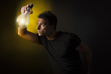 Concetto di pensiero ed immaginazione: uomo tiene tra le mani una lampadina accesa. Sfondo nero