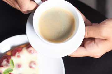 a cup of coffee in hand on the background of cake with strawberr