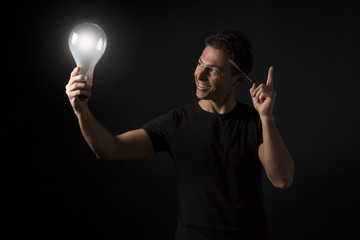 Ragazzo sorridente con indice alzato tiene una lampadina accesa: concetto di idea, ispirazione, creatività, innovazione